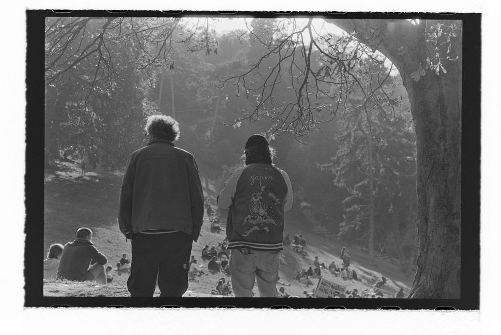A photo of two chaps stood in the park, slightly backlit by the late afternoon sun